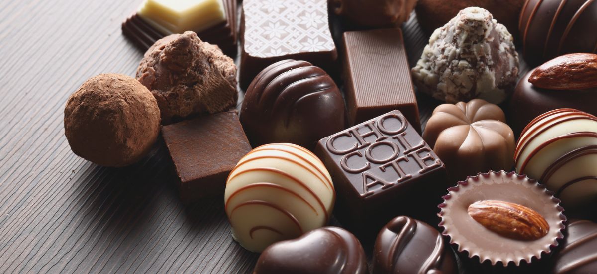 Chocolate Pode Ser Tóxico para Cães: Saiba Como Proteger Seu Amigo 1 Vários bombons e chocolates sortidos, incluindo trufas, quadrados e bombons decorados, dispostos sobre uma superfície de madeira.